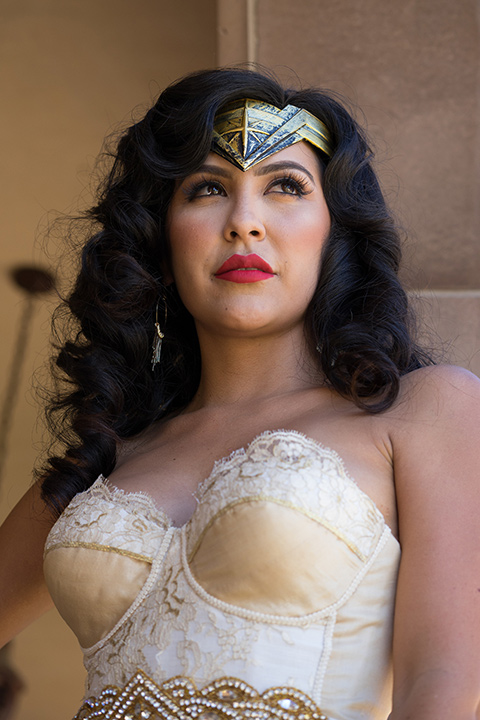 wonder-woman-close-up-bride-in-a-white-silk-dress-with-her-wonder-woman-head-piece-holding-onto-groom-in-a-navy-suit-and-red-long-tie-with-red-rose-florals