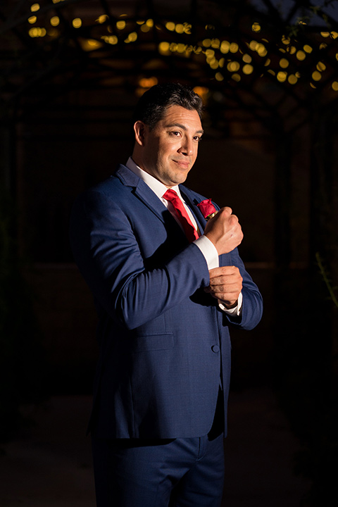 wonder-woman-meets-superman-groom-fixing-sleeve-to-the-side-groom-in-a-navy-suit-and-red-long-tie-with-red-rose-florals