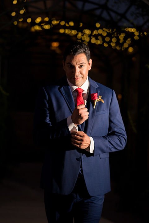 wonder-woman-meets-superman-groom-fixing-sleeve-groom-in-a-navy-suit-and-red-long-tie-with-red-rose-florals