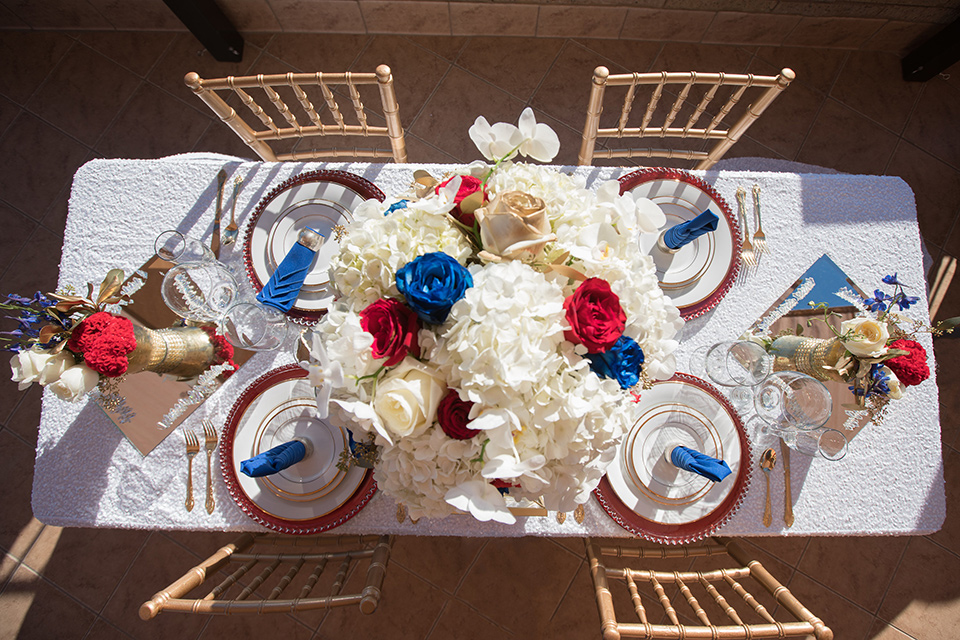 wonder-woman-meets-superman-placesetting-white-table-cloths-with-gold-chairs-and-accents-with-red-white-and-blue-florals-and-white-plates