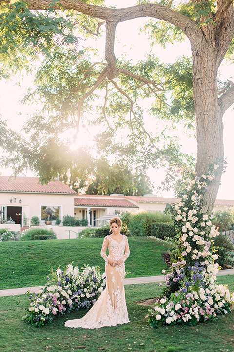 Inn-at-rancho-santa-fe-shoot-bride-by-tree-bride-in-a-lace-gown-with-an-illusion-detailing-with-a-nude-underlay-with-her-hair-in-back-in-a-loose-bun