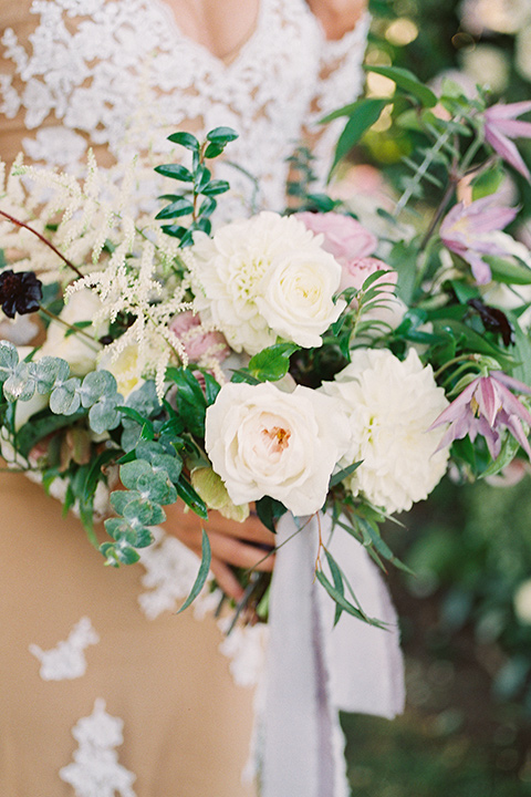 Inn-at-rancho-santa-fe-shoot-close-up-on-florals-bride-in-a-lace-gown-with-an-illusion-detailing-with-a-nude-underlay-with-her-hair-in-back-in-a-loose-bun-groom-in-a-black-tuxedo-with-black-blow-tie-and-a-white-and-black-polka-dot-pocket-square