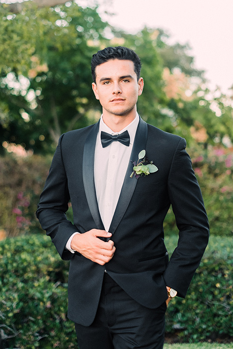 Inn-at-rancho-santa-fe-shoot-groom-along-standing-looking-straight-on-camera-groom-in-a-black-tuxedo-with-black-blow-tie-and-a-white-and-black-polka-dot-pocket-square