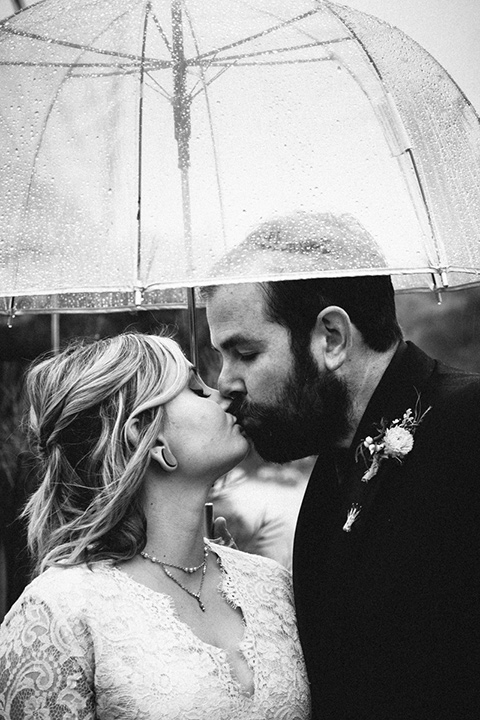 amanda-and-codys-wedding-at-the-1909-black-and-white-photo-with-umbrela-close-up-bride-in-an-a-line-dress-with-a-tulle-skirt-and-lace-long-sleeve-bodice-groom-in-all-black-shawl-lapel-tuxedo