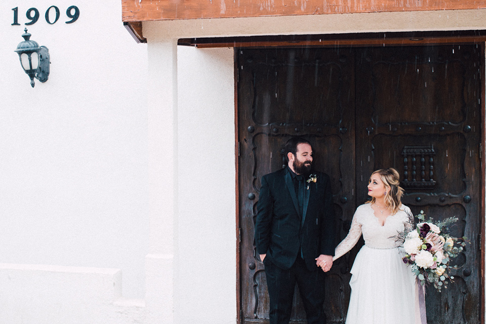 amanda-and-codys-wedding-at-the-1909-bride-and-groom-outside-1909-venue-looking-at-each-other-bride-in-an-a-line-dress-with-a-tulle-skirt-and-lace-long-sleeve-bodice-groom-in-all-black-shawl-lapel-tuxedo