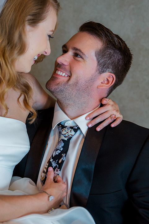 Childrens-museum-shoot-bride-and-groom-laughing-sitting-down-bride-in-a-white-modern-strapless-ball-gown-and-groom-in-a-black-tuxedo-with-a-floral-tie