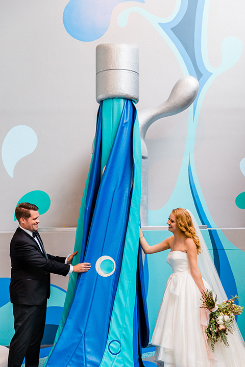 Childrens-museum-shoot-bride-and-groom-with-water-art-instilation-bride-in-a-white-modern-strapless-ball-gown-and-groom-in-a-black-tuxedo-with-a-floral-tie