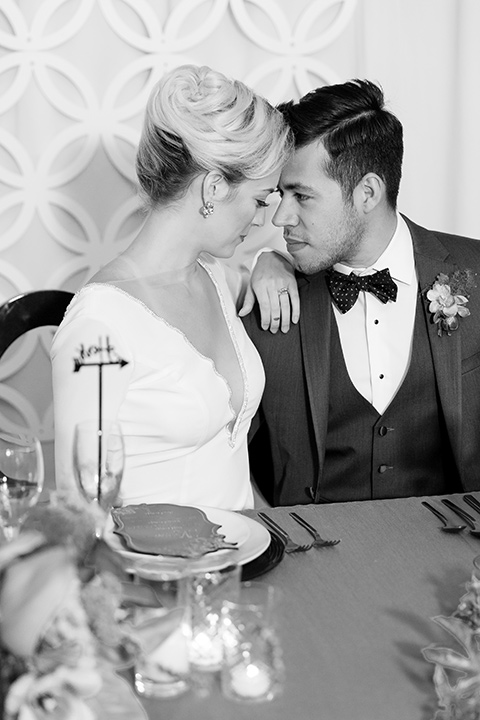 Exquisite-weddings-magazine-black-and-white-photo-of-bride-and-good-looking-at-each-other-bride-in-a-white-long-sleeved-dress-with-a-plunging-neckline-and-hair-in-a-bun-groom-in-a-grey-michael-kors-tuxedo-with-a-black-bowtie