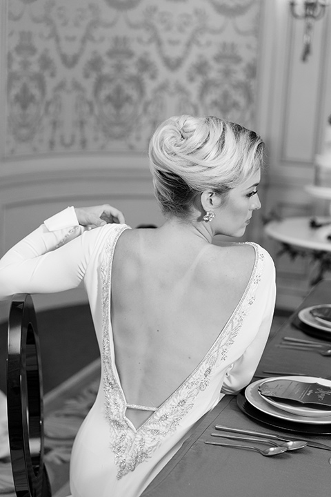 Exquisite-weddings-magazine-black-and-white-photo-of-detailing-on-bridal-gown-bride-in-a-white-long-sleeved-dress-with-a-plunging-neckline-and-hair-in-a-bun