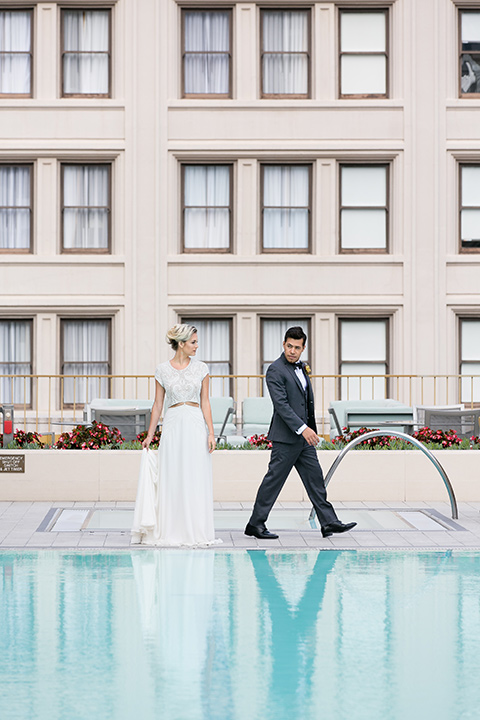 Exquisite-weddings-magazine-bride-and-groom-by-the-pool-bride-in-a-white-long-sleeved-dress-with-a-plunging-neckline-and-hair-in-a-bun-groom-in-a-grey-michael-kors-tuxedo-with-a-black-bowtie