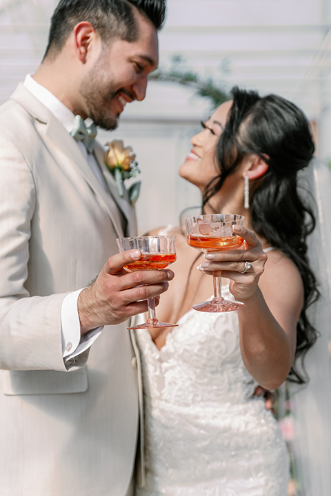  a garden romance wedding inspo with the bride in a luxe lace gown and the groom in a tan suit - drinking champagne 