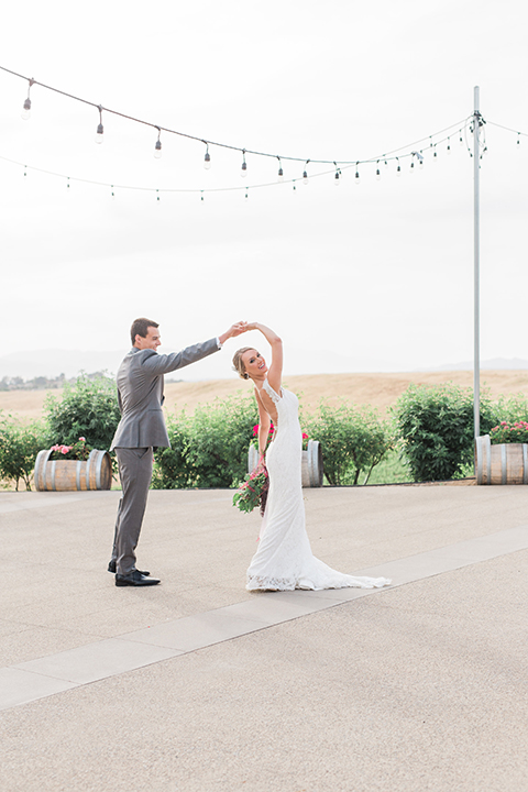 Temecula outdoor wedding at callaway winery bride form fitting lace gown with crystal beading and lace detail with open back design and beaded straps with groom grey notch lapel suit with matching vest and white dress shirt with long black skinny tie and pink floral boutonniere dancing