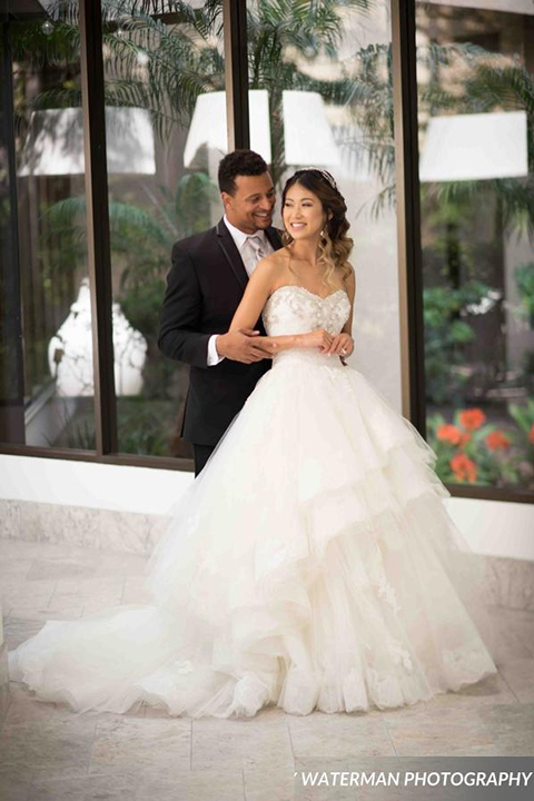 Classic glamour wedding shoot at the avenue of the arts hotel bride strapless ball gown with beaded detail on top with sweetheart neckline and groom black tuxedo with white dress shirt and long silver tie with matching vest and pocket square hugging