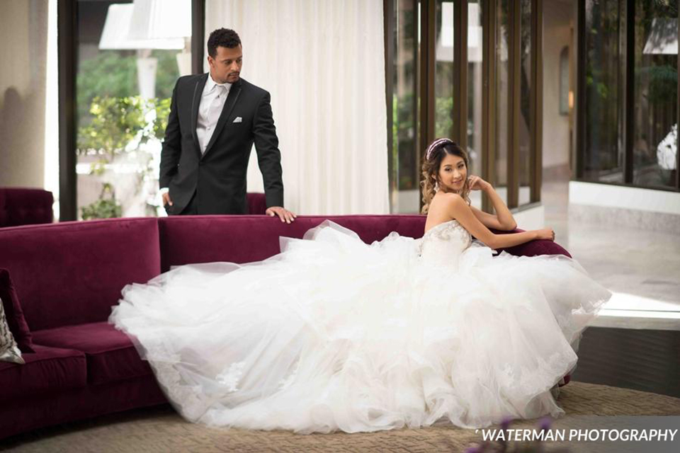 Classic glamour wedding shoot at the avenue of the arts hotel bride strapless ball gown with beaded detail on top with sweetheart neckline and groom black tuxedo with white dress shirt and long silver tie with matching vest and pocket square bride sitting on couch