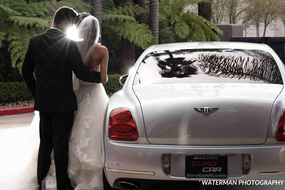 Classic glamour wedding shoot at the avenue of the arts hotel bride strapless ball gown with beaded detail on top with sweetheart neckline and groom black tuxedo with white dress shirt and long silver tie with matching vest and pocket square hugging by car