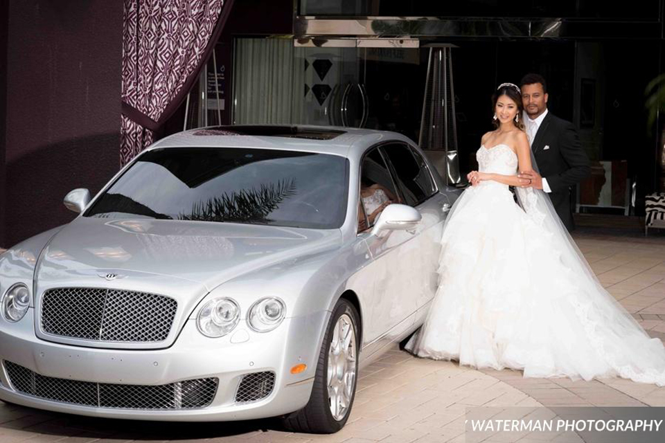 Classic glamour wedding shoot at the avenue of the arts hotel bride strapless ball gown with beaded detail on top with sweetheart neckline and groom black tuxedo with white dress shirt and long silver tie with matching vest and pocket square standing by car