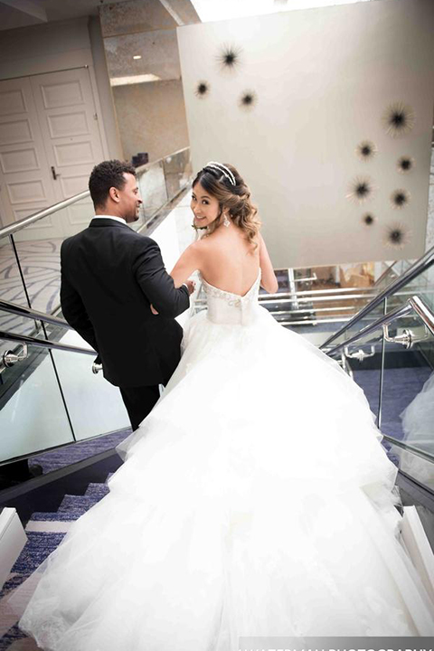 Classic glamour wedding shoot at the avenue of the arts hotel bride strapless ball gown with beaded detail on top with sweetheart neckline and groom black tuxedo with white dress shirt and long silver tie with matching vest and pocket square walking down stairs