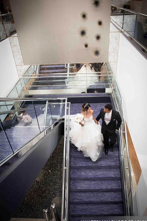Classic glamour wedding shoot at the avenue of the arts hotel bride strapless ball gown with beaded detail on top with sweetheart neckline and groom black tuxedo with white dress shirt and long silver tie with matching vest and pocket square walking down stairs