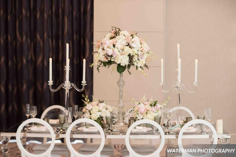 Classic glamour wedding shoot at the avenue of the arts hotel table set up with glass mirror table and white place settings with white and pink flower centerpiece decor with tall white candles and white chairs wedding photo idea for tables