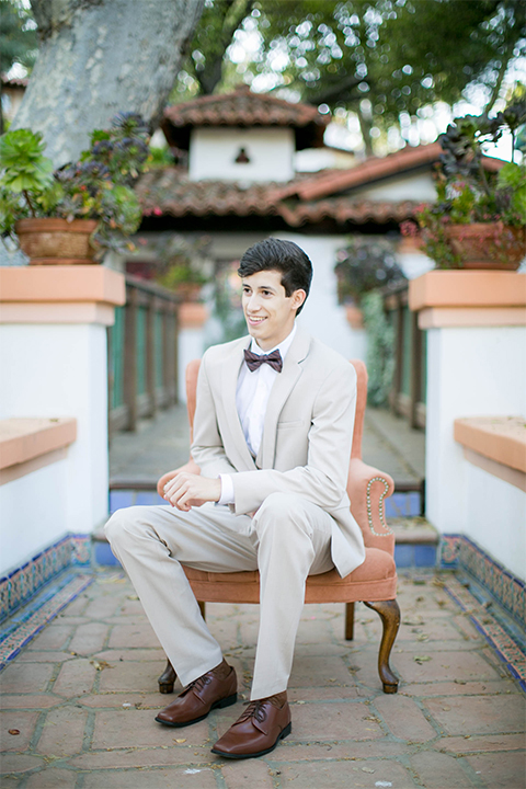 Rancho las lomas spanish inspired wedding shoot groom tan suit with matching vest and white dress shirt with dark grey bow tie sitting on chair