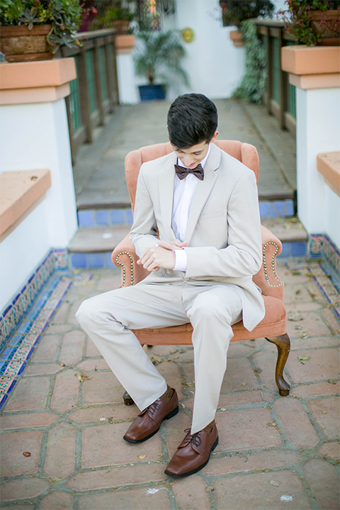 Rancho las lomas spanish inspired wedding shoot groom tan suit with matching vest and white dress shirt with dark grey bow tie sitting on chair