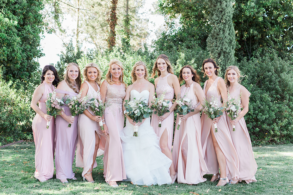 Temecula outdoor wedding at falkner winery bride mermaid style gown with lace bodice and sweetheart neckline with ruffled skirt and long veil holding white and green floral bridal bouquet with bridesmaids long blush pink dresses holding white and green floral bouquets