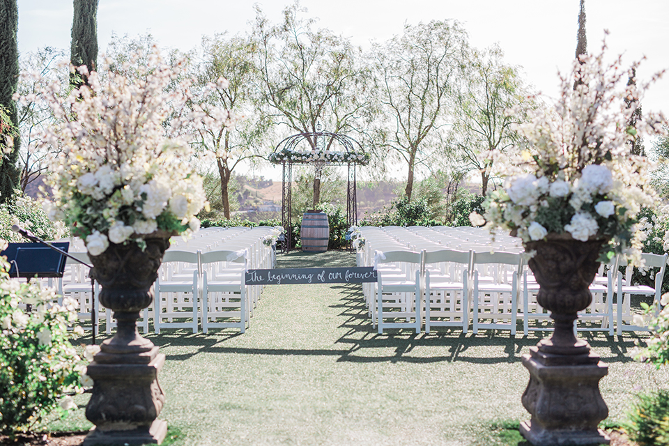 Temecula outdoor wedding at falkner winery ceremony set up on grass with white chairs and altar with flower decor and trees in background with sign at entrance wedding photo idea for ceremony