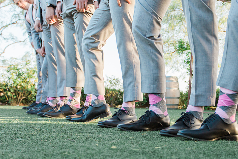 Temecula outdoor wedding at falkner winery groom heather grey suit with matching vest and white dress shirt with long white tie and matching pocket square with white floral boutonniere with groomsmen heather grey suits with long white ties and pink and grey plaid socks with black shoes