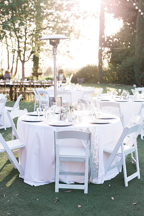 Temecula outdoor wedding at falkner winery reception set up with tables white table linen with white chairs and white place settings with pink and white name place and white flower decor with long light brown wood table with matching wood chairs and flower decor