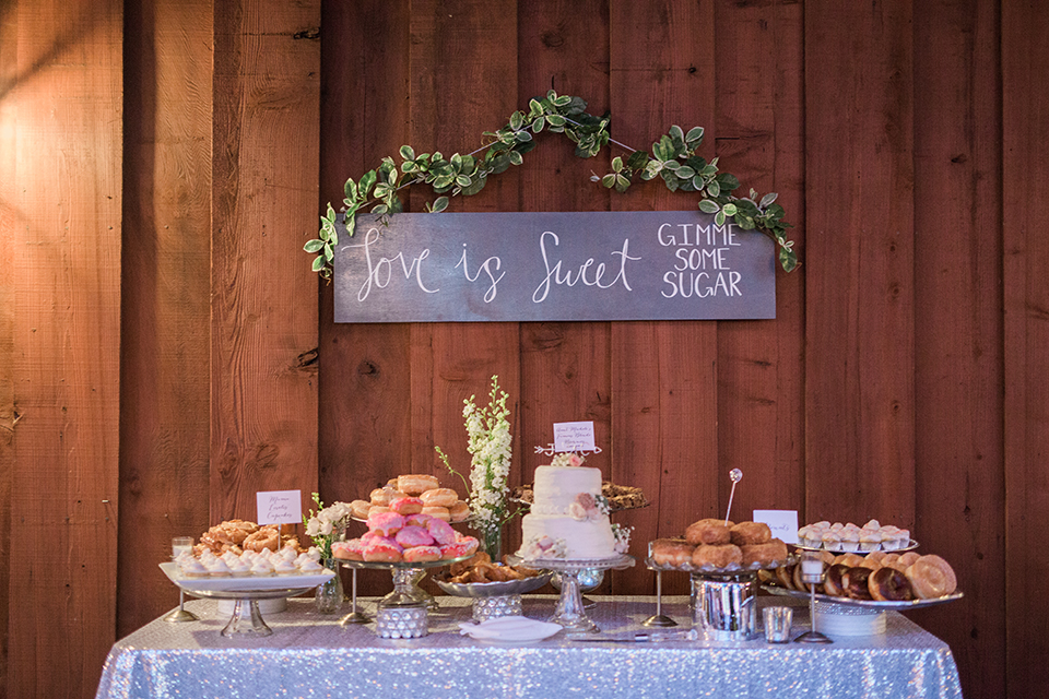 Temecula outdoor wedding at falkner winery reception set up with dessert table white linen with three tier white wedding cake on stand and assortment of donuts and treats with hanging sign and flower decor wedding photo idea for desserts