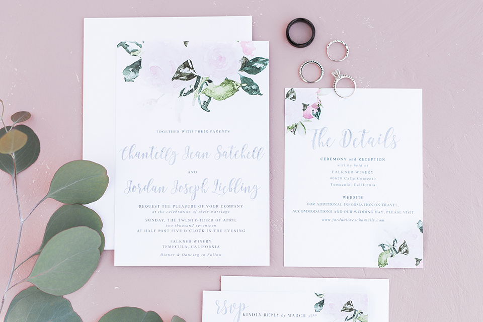 Temecula outdoor wedding at falkner winery wedding invitations white invitations with black calligraphy writing and greenery floral decor with wedding rings and light pink background wedding photo idea for invitations