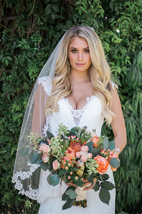 Orange county outdoor wedding at balboa bay resort bride form fitting lace gown with plunging neckline and lace straps with orange and green floral bridal bouquet 