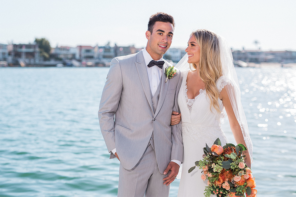 Balboa Bay Resort Wedding Bride and Groom Standing by Water Smiling with Flowers Grey Suit Navy Bow Tie
