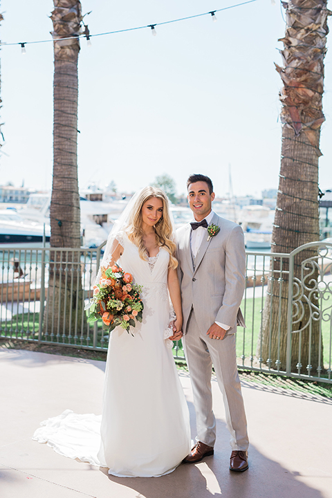 Balboa Bay Resort Wedding Bride and Groom Standing Holding Hands Near Water Grey Suit Navy Bow Tie Brown Shoes