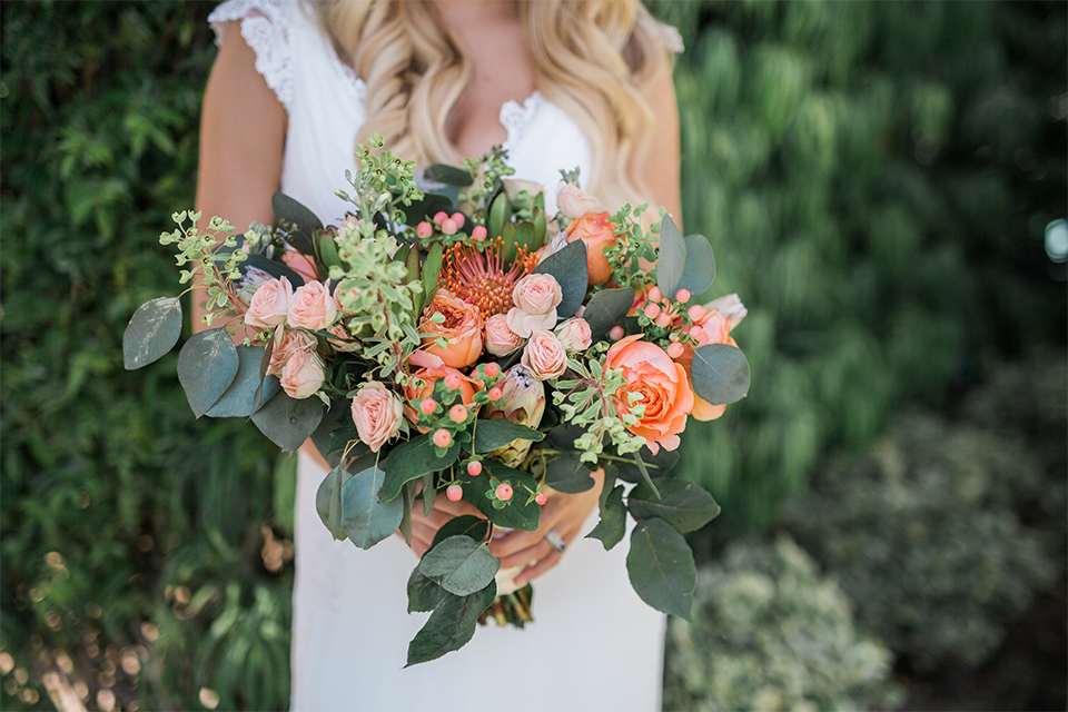 Orange county outdoor wedding at balboa bay resort bride form fitting lace gown with plunging neckline and lace straps with orange and green floral bridal bouquet close up