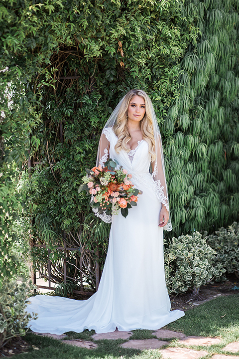Orange county outdoor wedding at balboa bay resort bride form fitting lace gown with plunging neckline and lace straps with orange and green floral bridal bouquet 