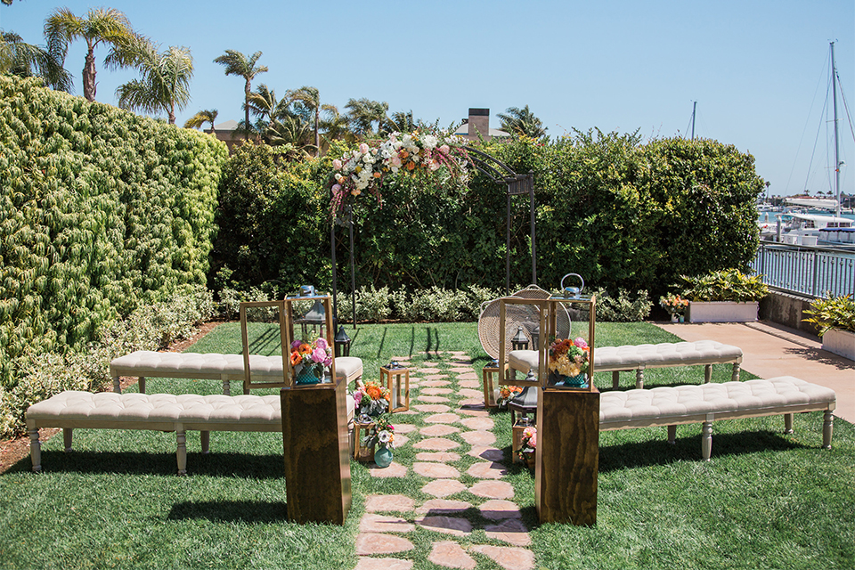 Orange county outdoor wedding shoot at balboa bay resort ceremony set up with white benches and chairs with stone aisle on grass with pillars and flower decor wedding photo idea for ceremony