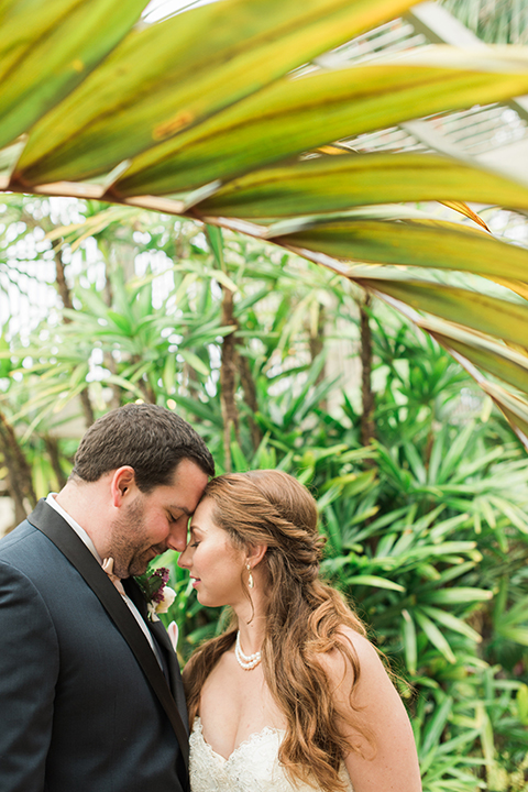 Orange county outdoor wedding at sherman library and gardens bride form fitting strapless lace gown with sweetheart neckline and pearl necklace with groom navy blue shawl lapel tuxedo with matching vest and white dress shirt with blush pink bow tie and white floral boutonniere hugging