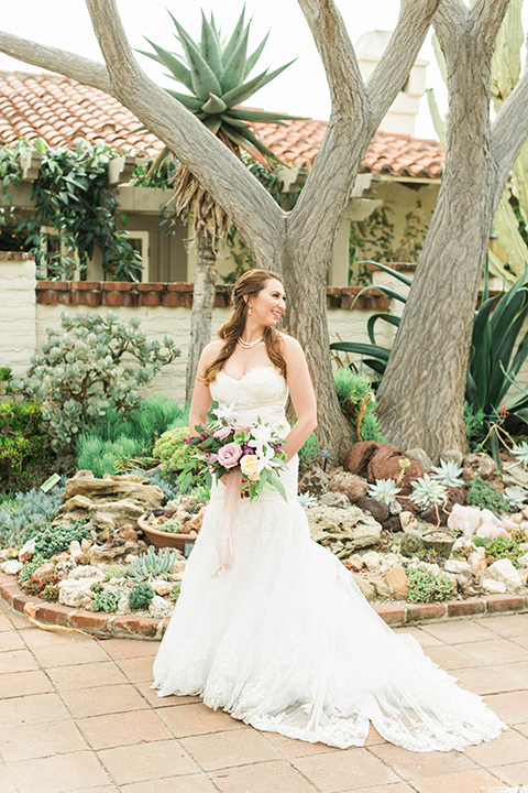 Orange county outdoor wedding at sherman library and gardens bride form fitting strapless lace gown with sweetheart neckline and pearl necklace holding white and pink floral bridal bouquet