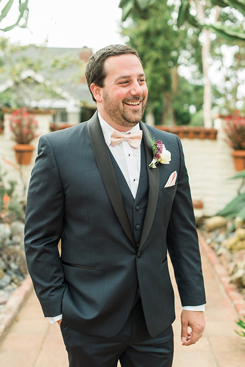 Orange county outdoor wedding shoot at sherman library and gardens groom navy blue shawl lapel tuxedo with matching vest and white dress shirt with blush pink bow tie and pocket square with white floral boutonniere