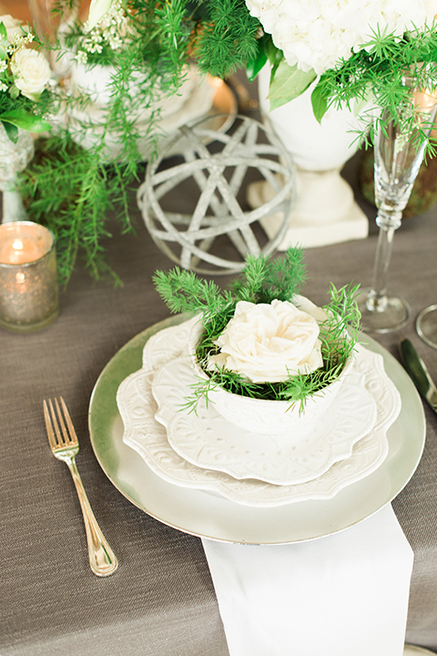 Orange county outdoor wedding shoot at sherman library and gardens table set up with light grey table linen and white place settings with green and white flower centerpiece decor with gold silverware and light brown and white wood chairs