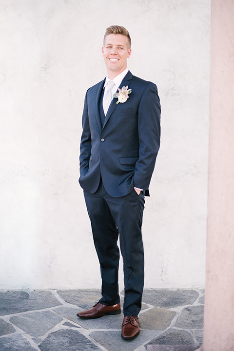 Orange county outdoor wedding shoot at old ranch country club groom navy blue notch lapel suit with matching vest and white dress shirt with long silver tie and white floral boutonniere standing with hands in pockets