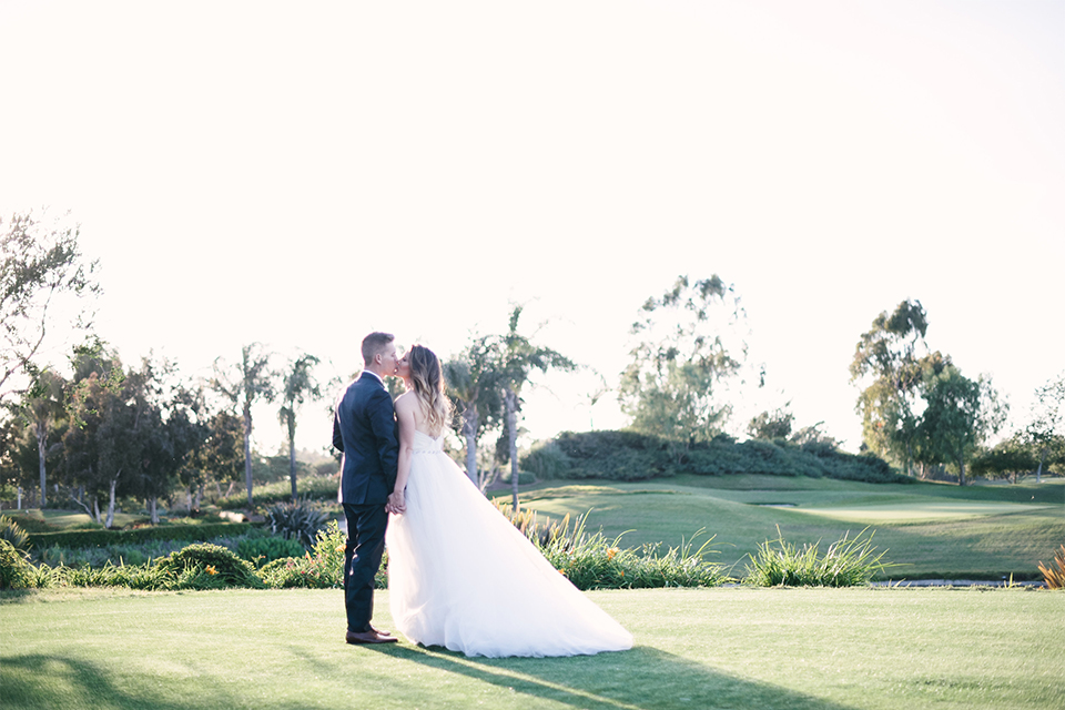 Orange county outdoor wedding at old ranch country club bride strapless ballgown with a sweetheart neckline and beaded detail with groom navy notch lapel suit with matching vest and white dress shirt with long silver tie and white floral boutonniere kissing