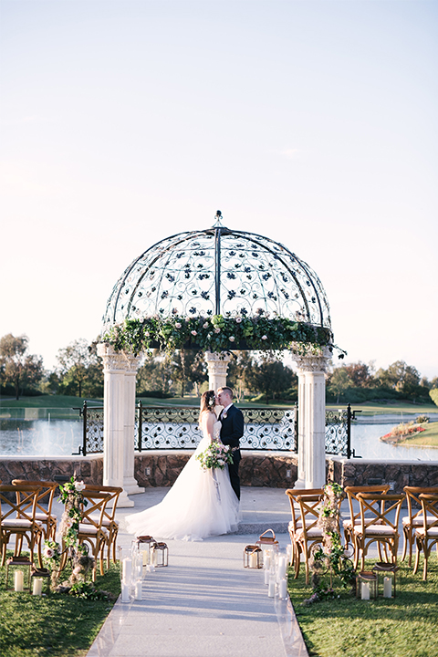 Orange county outdoor wedding at old ranch country club bride strapless ballgown with a sweetheart neckline and beaded detail with groom navy notch lapel suit with matching vest and white dress shirt with long silver tie and white floral boutonniere standing during ceremony bride holding light pink and green floral bridal bouquet