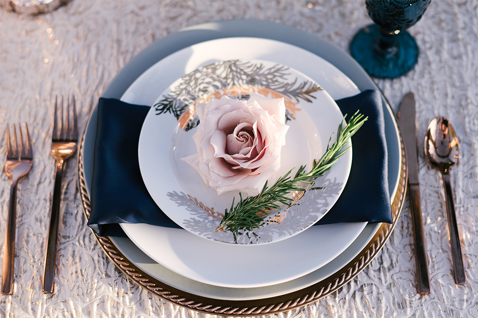 Orange county outdoor wedding shoot at old ranch country club table set up light silver table linen with white and grey place settings with navy blue napkin linen decor with clear wine glasses and dark blue designed glasses with light pink flower centerpiece decor with candles