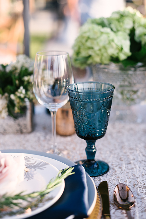 Orange county outdoor wedding shoot at old ranch country club table set up light silver table linen with white and grey place settings with navy blue napkin linen decor with clear wine glasses and dark blue designed glasses with light pink flower centerpiece decor with candles
