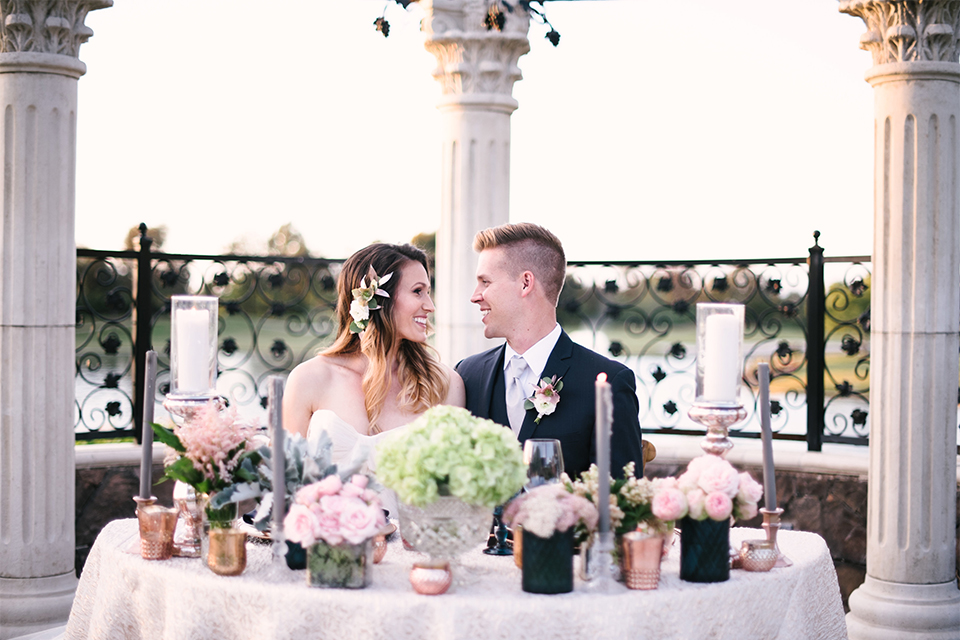 Orange county outdoor wedding at old ranch country club bride strapless ballgown with a sweetheart neckline and beaded detail with groom navy notch lapel suit with matching vest and white dress shirt with long silver tie and white floral boutonniere sitting at table smiling