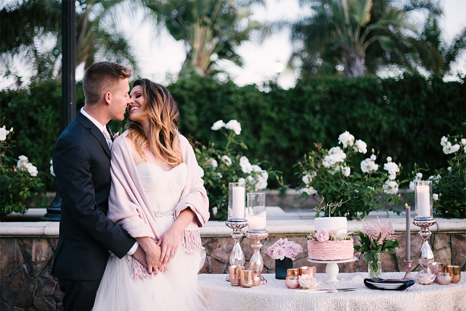 Orange county outdoor wedding at old ranch country club bride strapless ballgown with a sweetheart neckline and beaded detail with groom navy notch lapel suit with matching vest and white dress shirt with long silver tie and white floral boutonniere standing by cake table