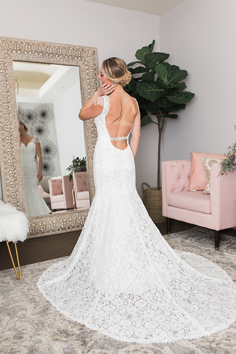 Temecula outdoor wedding at callaway winery bride form fitting lace gown with crystal beading and lace detail with open back design and beaded straps looking in mirror getting ready before ceremony