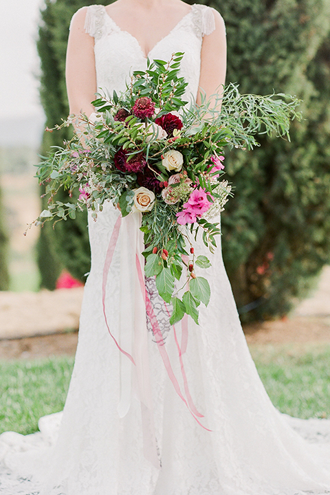 Temecula outdoor wedding at callaway winery bride form fitting lace gown with crystal beading and lace detail with open back design and beaded straps holding pink and green floral bridal bouquet